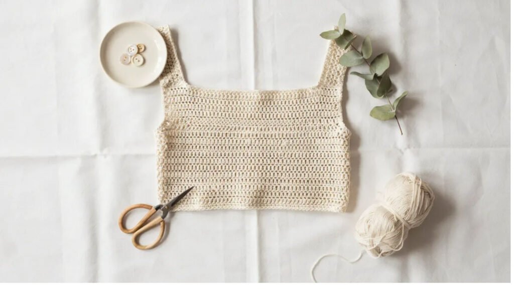 Handmade ivory crochet crop top with simple rectangle construction and double crochet stitches displayed as a flat lay on white linen