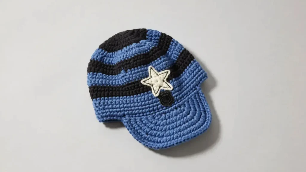 A blue and black crochet police-style beanie hat with a brim and a star applique, laid flat on a neutral surface.