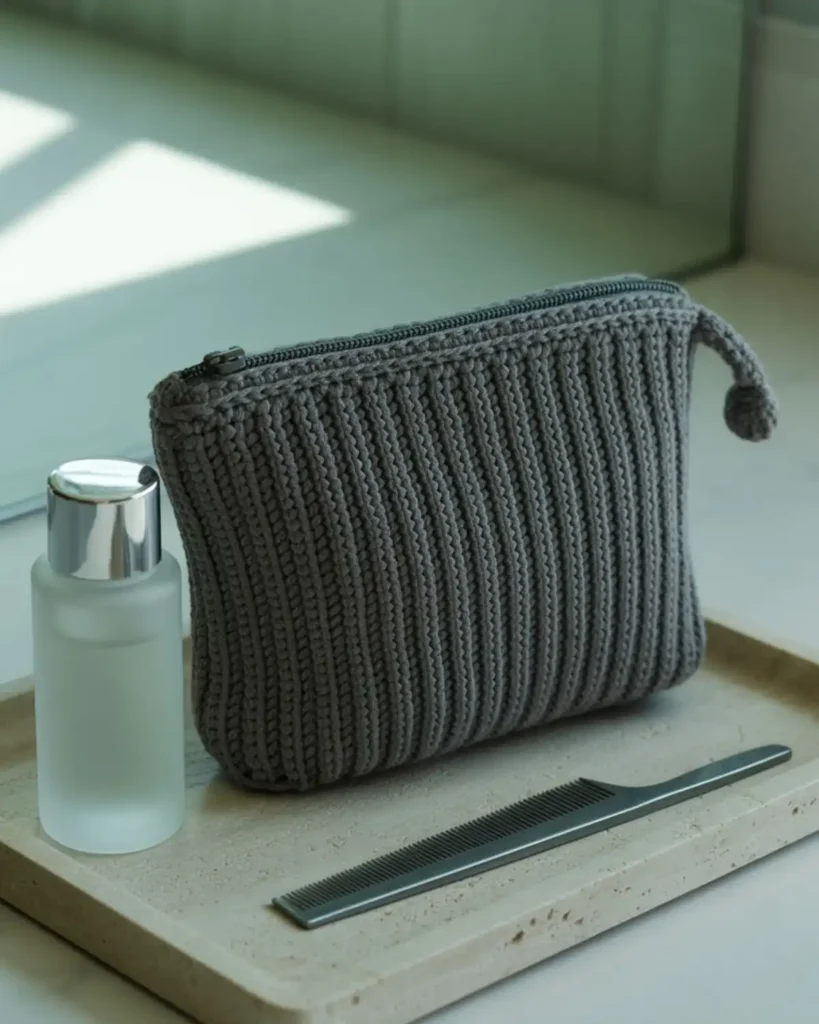 Charcoal ribbed crochet makeup pouch with a matching zipper on a stone tray.