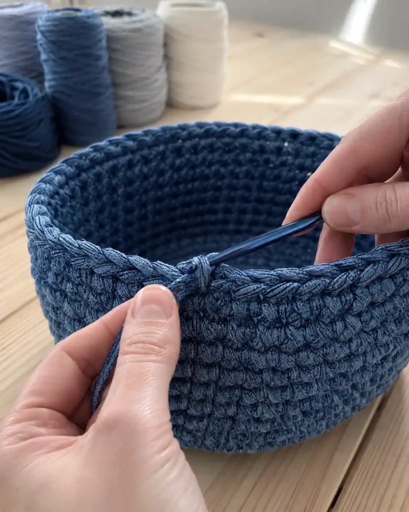Blue crochet basket being finished with a cord-like crab stitch border.