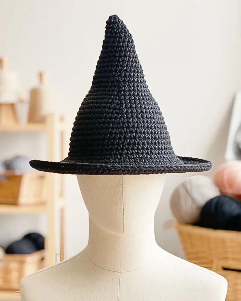  Black crochet witch hat with a compact short brim and neat pointed crown.