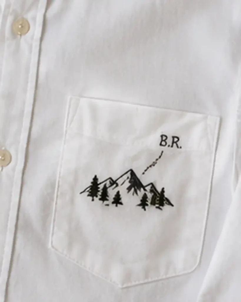 White cotton shirt with a tiny blue embroidered wave motif beside the chest pocket.