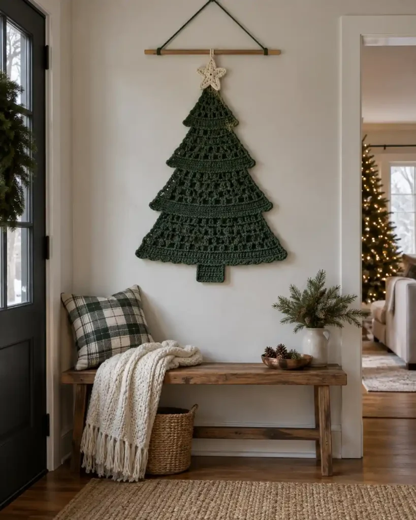 A flat forest-green crochet Christmas tree wall hanging with an ivory star on a natural wooden dowel above a narrow entryway bench.