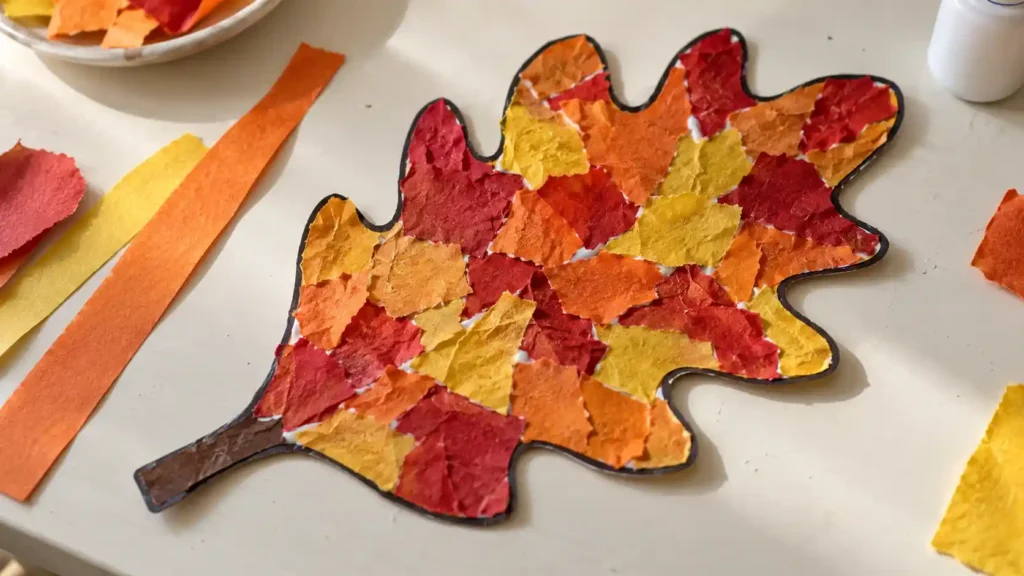 A large oak-leaf outline filled with irregular red, orange and yellow torn paper, visible glue marks and rough paper edges.