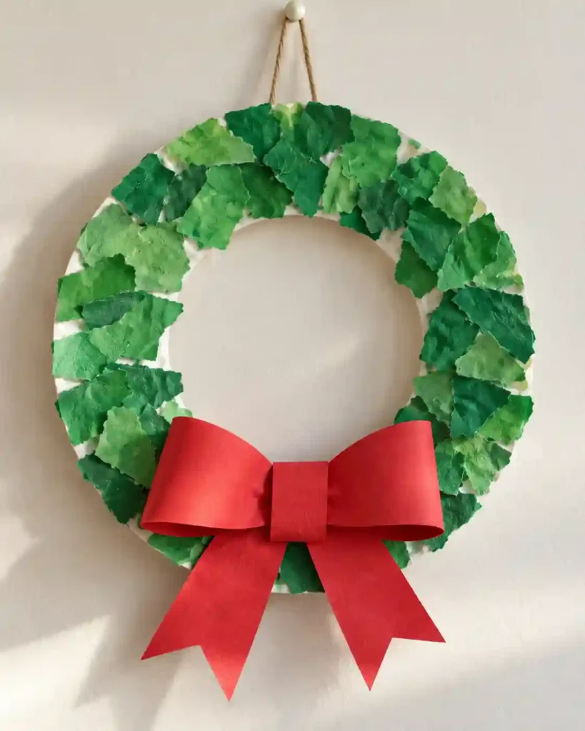 A large cardstock tree covered in overlapping green tissue squares and oversized red paper circles on a preschool art tray.