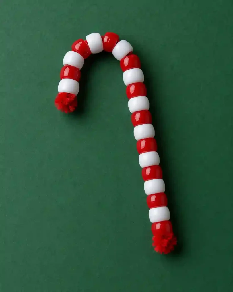 A red and white pony-bead candy cane with tightly folded chenille-stem ends resting on a plain evergreen-colored background.