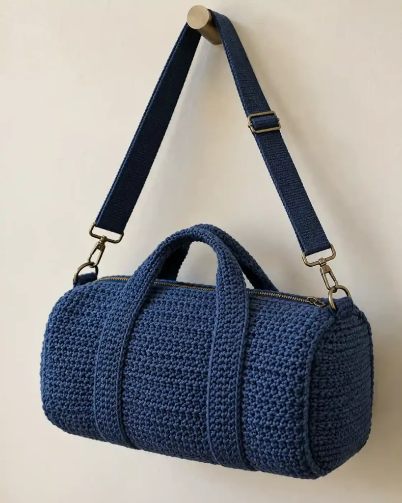 Detachable Shoulder-Strap Crochet Duffle showing a dark denim-blue crochet rectangular duffle with an adjustable detachable wide shoulder strap clipped to metal side rings.
