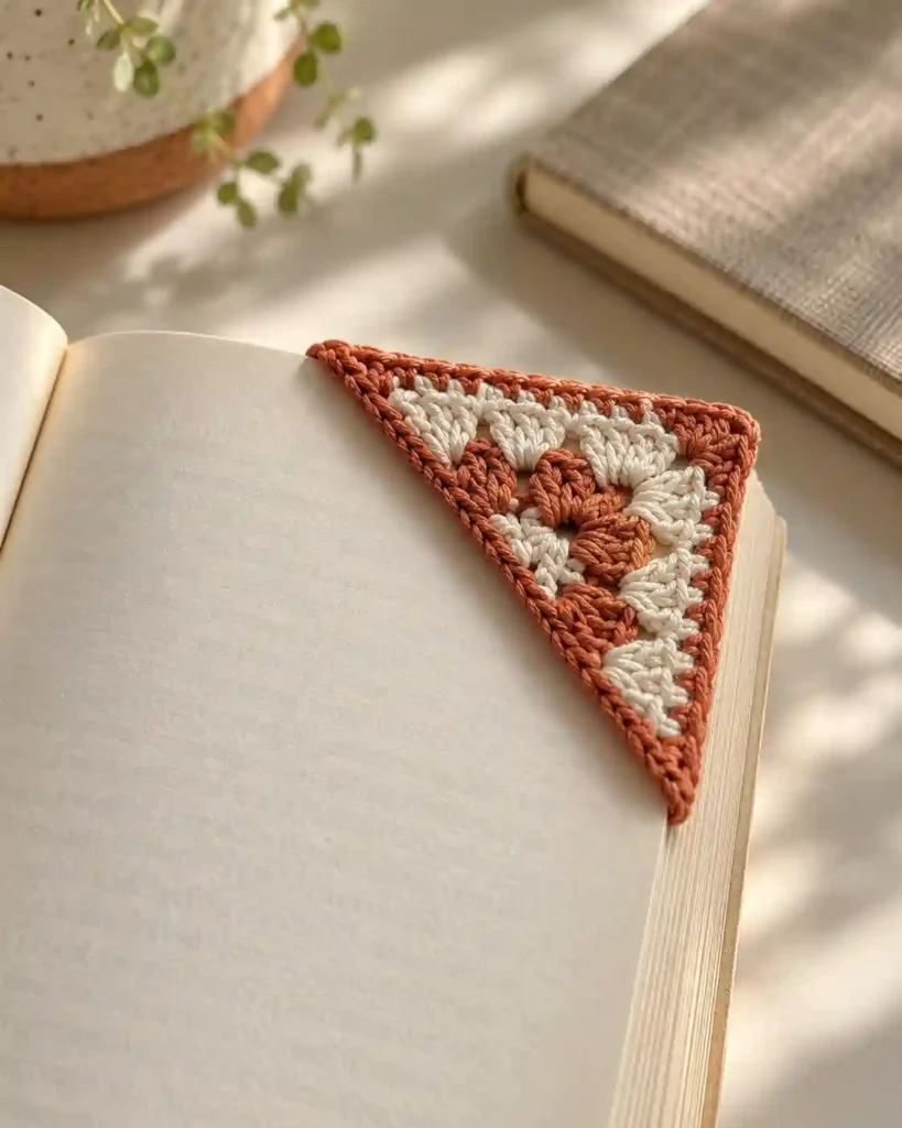 Two-tone triangle crochet bookmark slipped over the corner of one page.