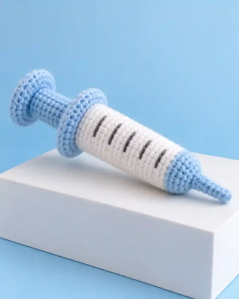 Landscape editorial photo of a pink-and-cream capsule-shaped crochet keychain with minimal stitched smile beside a key ring; crochet chill pill keychain, realistic visible crochet stitch detail.